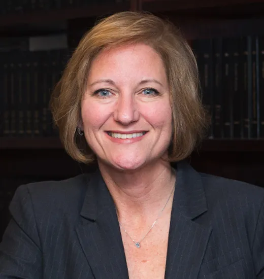 A professional woman in a suit and tie seated at a desk, focused on her work with a confident demeanor.