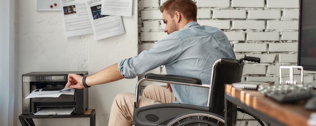 A man in a wheelchair operates a printer, showcasing accessibility in technology and office environments.