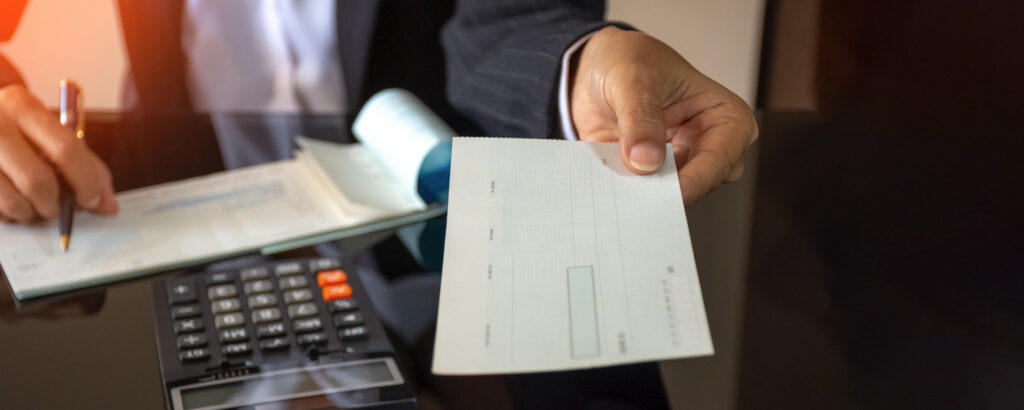 A man in a suit holds a check in one hand and a calculator in the other, focused on financial calculations.