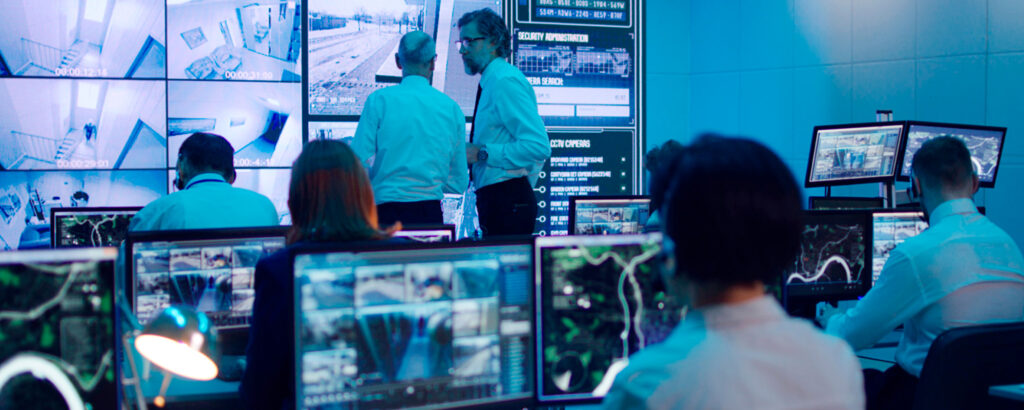 A diverse group of individuals collaborating in front of several computer monitors, engaged in a discussion.