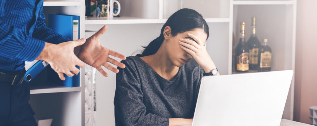 A man and woman sit at a desk, both with their hands on their heads, appearing deep in thought or stressed.