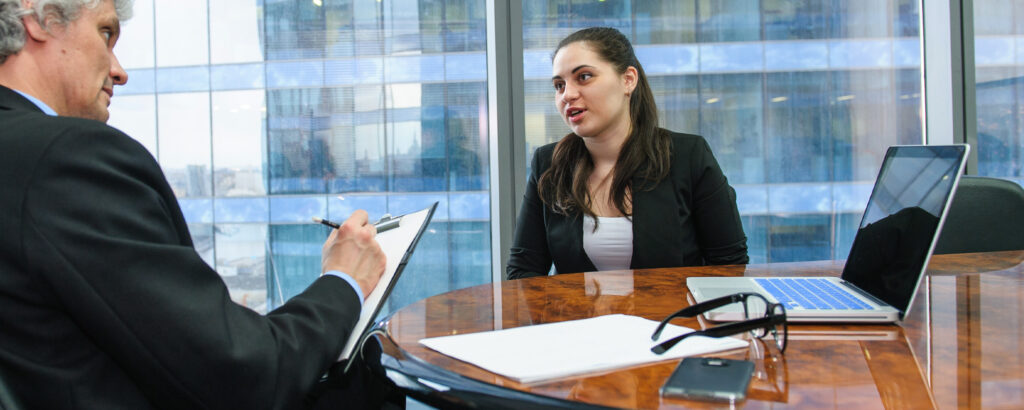 A man and woman seated at a table, focused on a laptop in front of them.