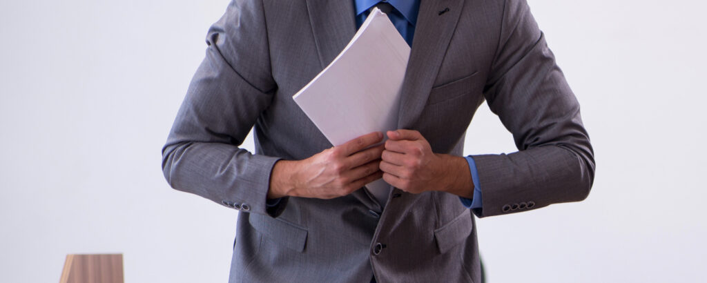 A man in a suit stands confidently, holding a piece of paper in his right hand, ready to present information.