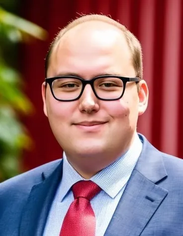 A man wearing glasses and a red tie, looking confidently at the camera.