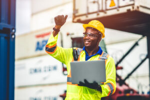 happy worker working in logistic shipping with laptop computer control loading containers at port cargo. Import export shipping industry people.