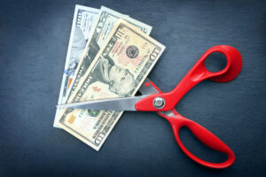 Red scissors cut money on black background. Financial concept